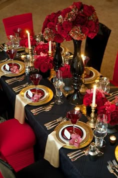 the table is set with black and gold plates, silverware, red flowers, and candles