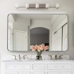 a bathroom vanity with two sinks and a large mirror above it that has flowers in the vase