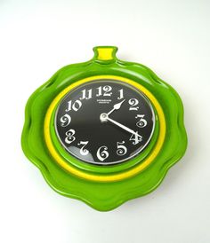 a green and yellow clock with numbers on it's face sitting on a white surface