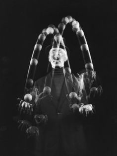 a black and white photo of a man with his hands in front of him, surrounded by balls