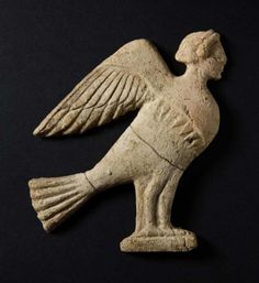 an ancient figurine of a bird with outstretched wings on a black background,