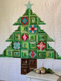 a quilted christmas tree is displayed on a table next to a white dresser and wall