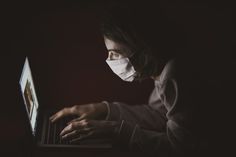 a woman wearing a face mask and using a laptop in the dark with her hands