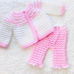 three crocheted sweaters and pants are laying on a white blanket with pink trim