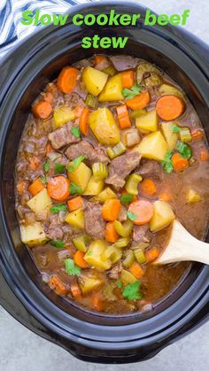 a crock pot filled with beef stew and carrots next to a blue towel