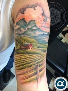 a man's arm with a farm scene on it and clouds in the sky