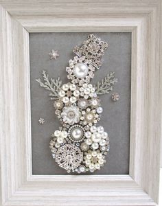 a snowman made out of pearls and other ornaments in a white frame with silver trim