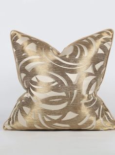 a gold and white pillow with an intricate design on the front, sitting on a white surface