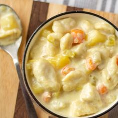 a bowl filled with chicken and dumplings next to a spoon on a cutting board