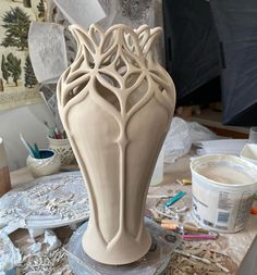 a vase sitting on top of a table covered in paint and paper work next to other crafting supplies