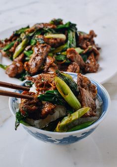 two plates filled with meat, vegetables and chopsticks on a marble table top