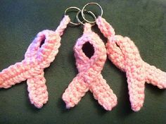 three crocheted pink ribbon shaped keychains sitting on top of a table