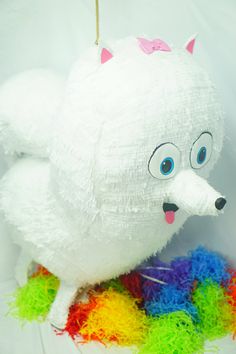 a white stuffed animal with blue eyes and pink nose sitting on top of a rainbow colored ball