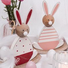 two wooden rabbits sitting next to each other on top of a table with pink flowers