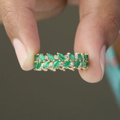 a close up of a person's hand holding a ring with emeralds and diamonds