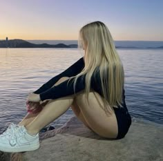 a woman sitting on top of a rock next to the ocean with her legs crossed