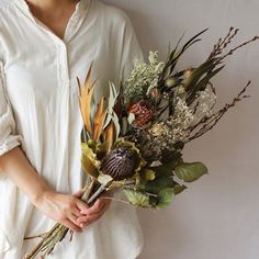 a woman holding a bouquet of flowers in her hands and wearing a white shirt with long sleeves