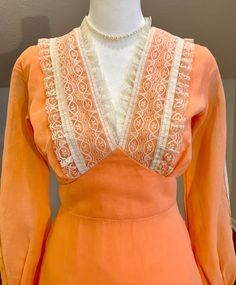 "Lovely apricot/peach color prairie dress with cream color lace trim. This 70's dress is in amazing vintage condition! There is a small amount of fraying on the side where the tie sash meets the waistband. It isn't really noticeable but please see the last photo for details. There is no maker's tag but there is a dry clean only tag stitched into the back lower lining of the dress. This dress looks handmade otherwise.  Zips up the back and ties with sash. Hook and eyes. Snaps at the wrist.  Measurements taken flat and are approximate. Please measure carefully as I don't take refunds but feel free to message me with any questions. Waist: 13\" (x2) Bust: 17\" (x2) blousy top Hips: 18\" (x2) Length: 54\" Sleeve length: 22\" Would best fit a size Small" Vintage Beige Prairie Dress For Spring, Vintage Apricot Dress For Spring, Spring Vintage Dress With Lace Trim, Orange Vintage Dress For Spring, Retro Prairie Dress With Lace Trim For Spring, 70s Inspired Orange Summer Dress, Fitted Cottagecore Prairie Dress, 70’s Dresses Unique Vintage, Vintage Prairie Dress With Lace Trim For Summer