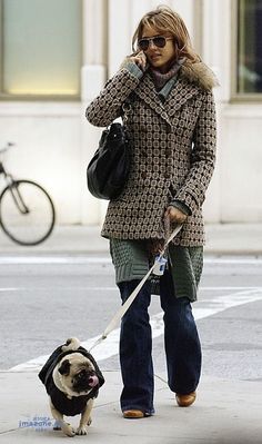 a woman walking her dog on a leash down the street while talking on a cell phone