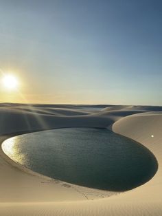 the sun shines brightly over an expanse of sand dunes and water in the foreground