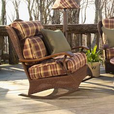 two wicker rocking chairs with plaid cushions on a deck in front of some trees