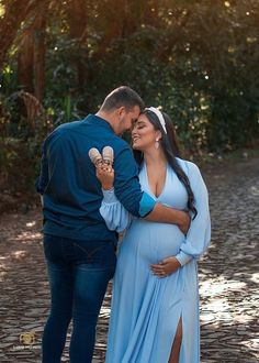 a pregnant woman in a blue dress holding an ice cream cone while standing next to a man