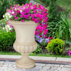 pink and white flowers are in a large flower pot on the side of a brick walkway