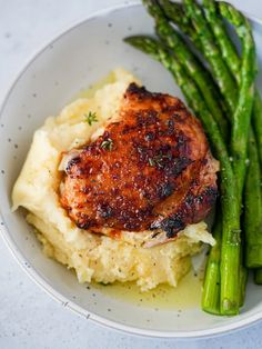 a white plate topped with mashed potatoes and asparagus next to a piece of meat