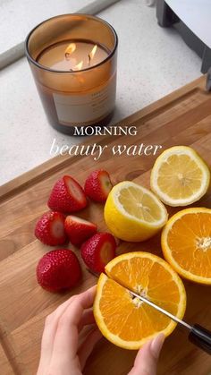 someone cutting up oranges and strawberries on a cutting board with a candle in the background