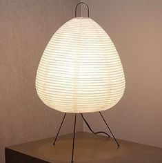 a white lamp sitting on top of a wooden table next to a black box and wall