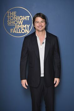 a man in a black suit and white shirt smiles at the camera while standing next to a blue wall