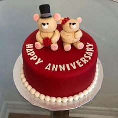 two teddy bears are sitting on top of a red and white cake that says happy anniversary