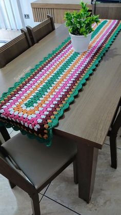 a crocheted table runner sitting on top of a wooden table next to a potted plant