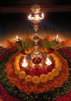 a lit diya with flowers and candles in the center on a circular table cloth