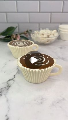 three white cups filled with chocolate sitting on top of a marble counter next to flowers