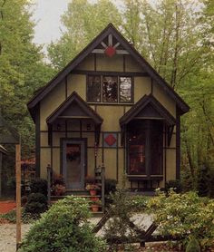 a small house in the middle of some trees and bushes, with a red heart on it's front door