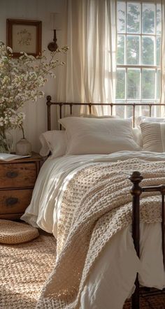 a bed sitting under a window next to a dresser with flowers on top of it