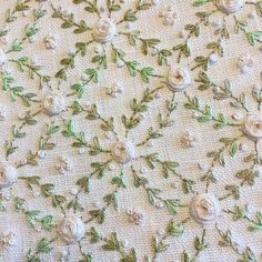 an embroidered fabric with white flowers and green leaves on the bottom, along with pearls