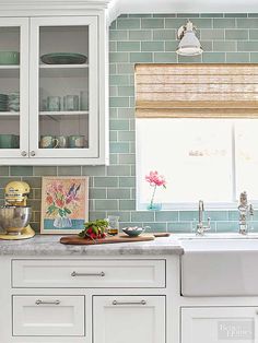 a kitchen with white cabinets and green tile backsplashing on the window sill