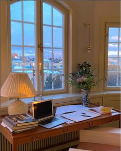 a laptop computer sitting on top of a wooden desk in front of two large windows