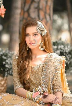 a woman with long brown hair wearing a gold dress and jewelry is posing for the camera