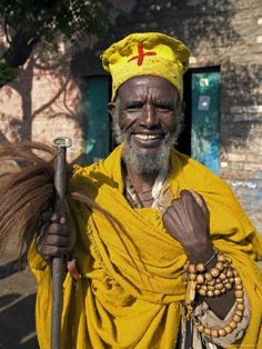 a man in yellow is holding a stick and smiling at the camera while standing outside