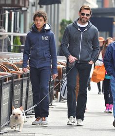 a man and woman walking their dog on a leash down a sidewalk with other people