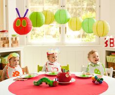 three children sitting at a table with birthday hats on and decorations hanging from the ceiling