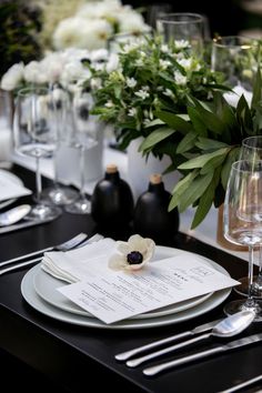 the table is set with place settings, silverware and flowers in black vases