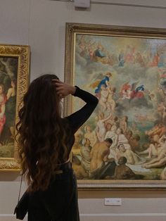 a woman standing in front of a painting with her back to the camera and looking at it