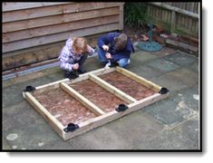 two people are working on some kind of wooden structure in the yard with wood planks laid out around them