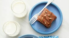 a piece of chocolate cake on a blue plate next to two cups and a fork