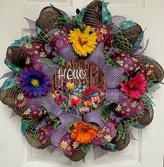 a purple wreath with flowers and the word hello written on it in front of a white door