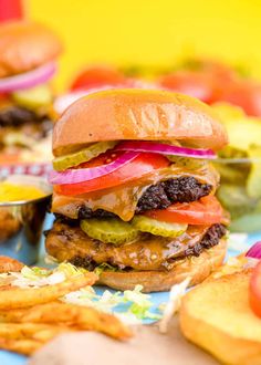 two hamburgers and fries on a blue tablecloth with yellow wall in the background